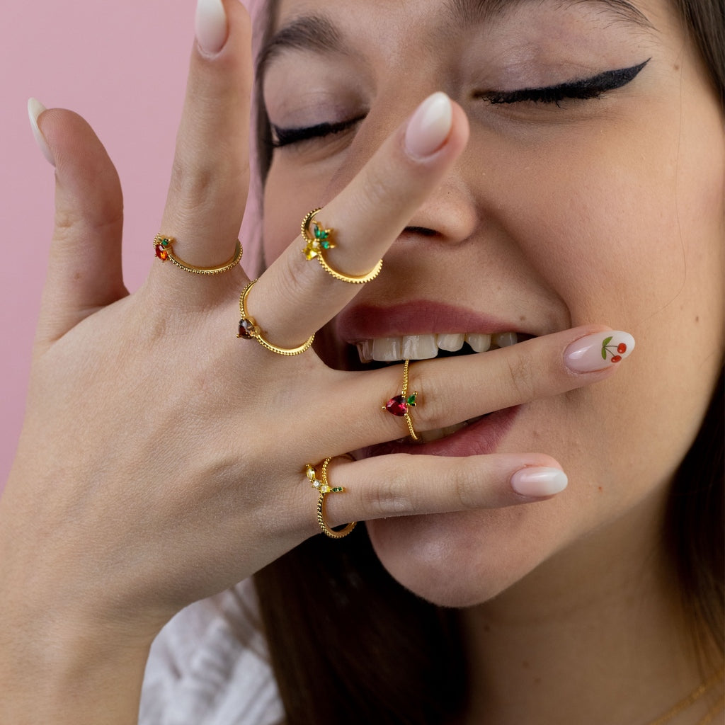 Anelli con charms fruttati in oro 18 carati indossati su mani femminili – gioielli moda estate 2025 Fruits & Jewels