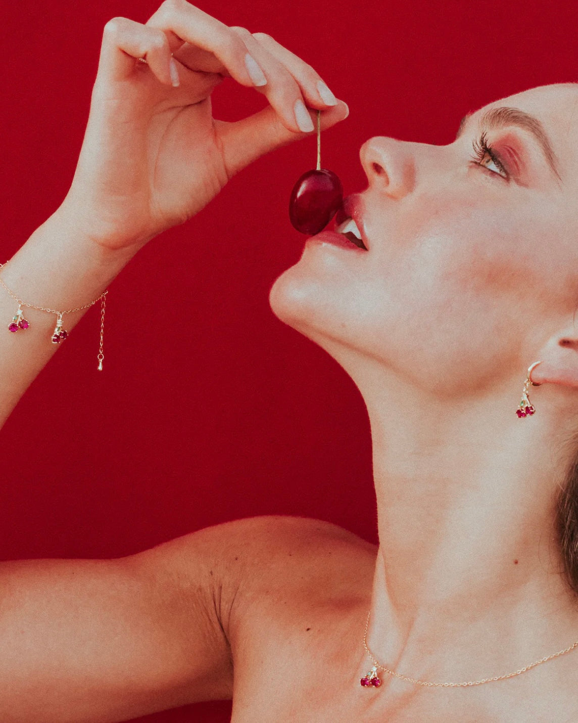 Orecchino ciliegia placcato oro 18 carati visibile mentre la modella porta alla bocca una ciliegia – atmosfera sensuale e fruttata Fruits & Jewels