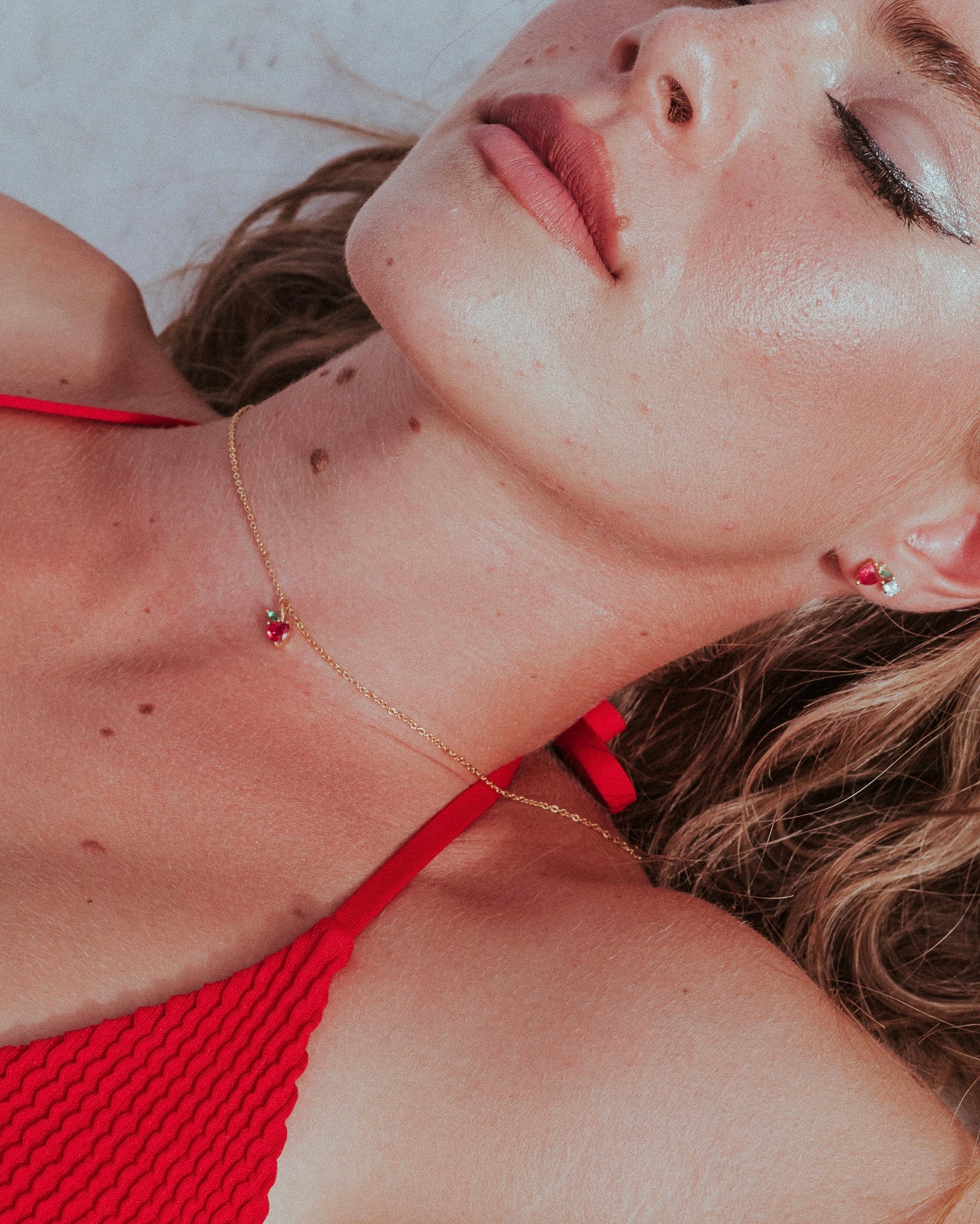 Scatto dall’alto della collana pendente mela indossata da modella sdraiata al sole, Fruits & Jewels