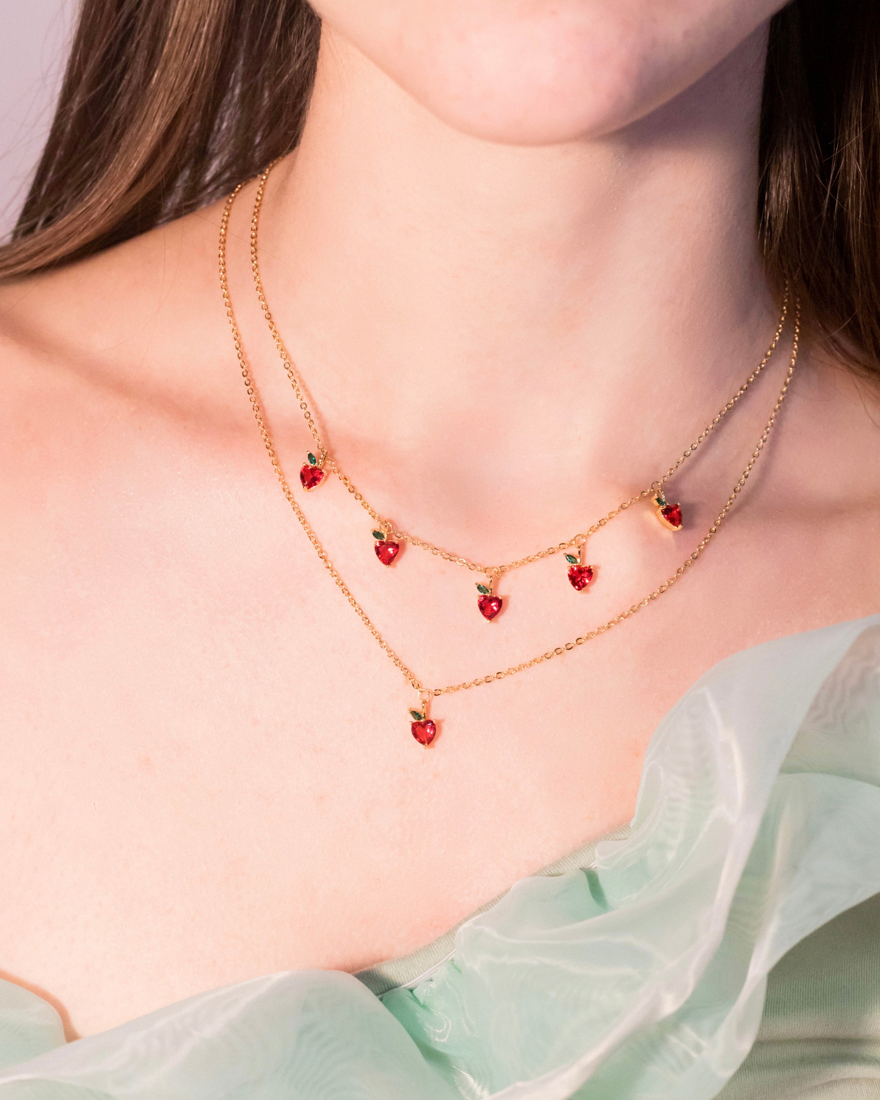 Primo piano della collana con charms mela placcata in oro 18 carati indossata su abito verde chiaro, Fruits & Jewels