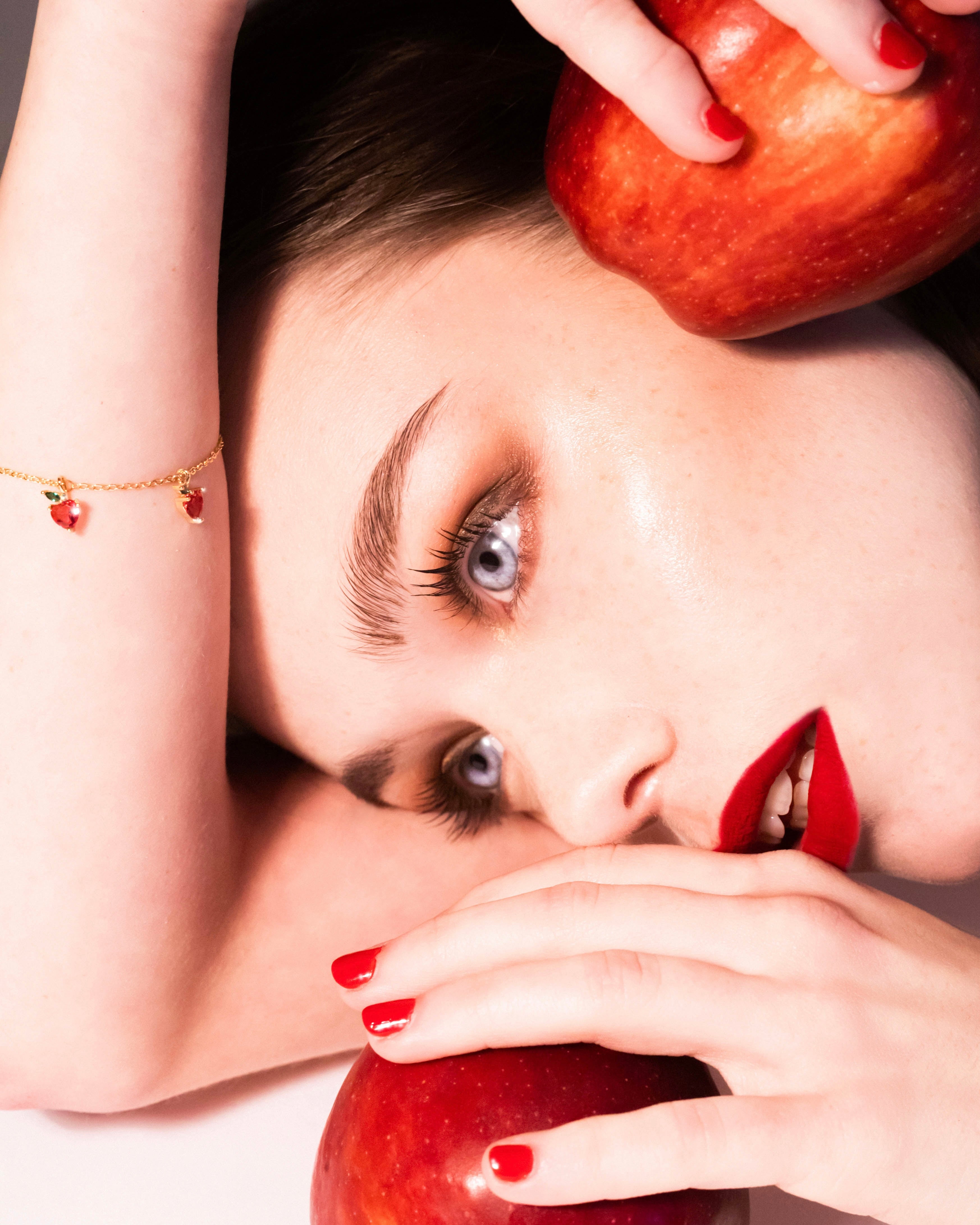 Bracciale mela oro 18 carati indossato con rossetto rosso acceso e mela rossa, Fruits & Jewels