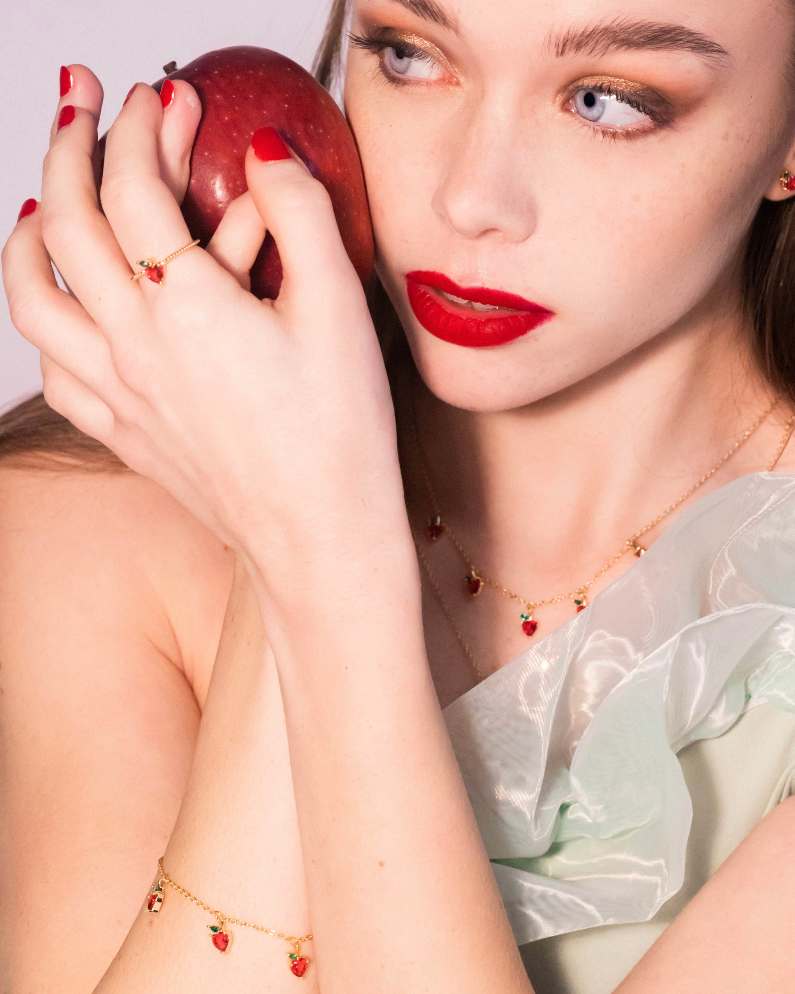 Bracciale mela placcato oro 18 carati abbinato a collana, con modella che tiene una mela, Fruits & Jewels