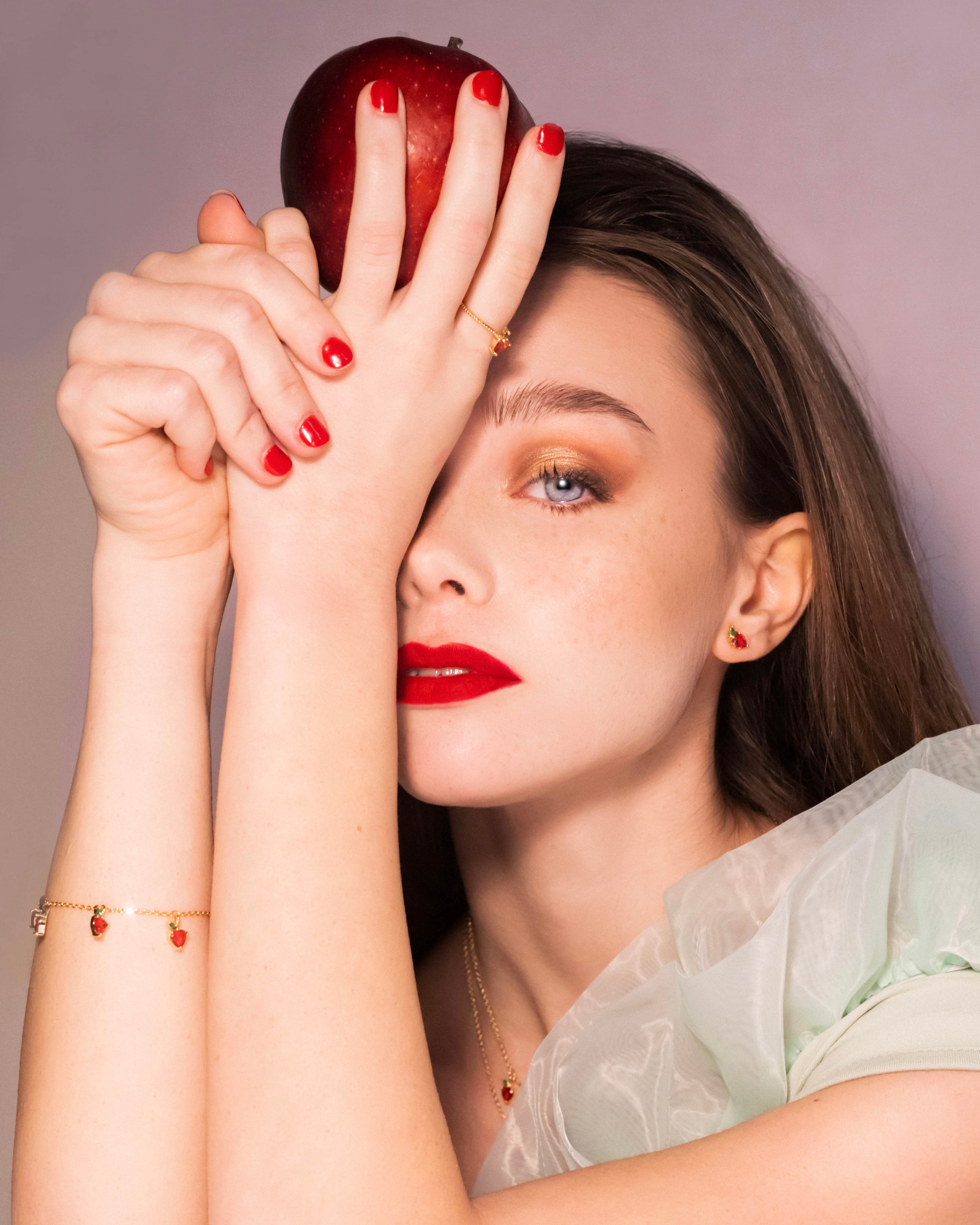 Modella con bracciale mela oro 18 carati, mano sollevata e mela rossa appoggiata sulla fronte, Fruits & Jewels