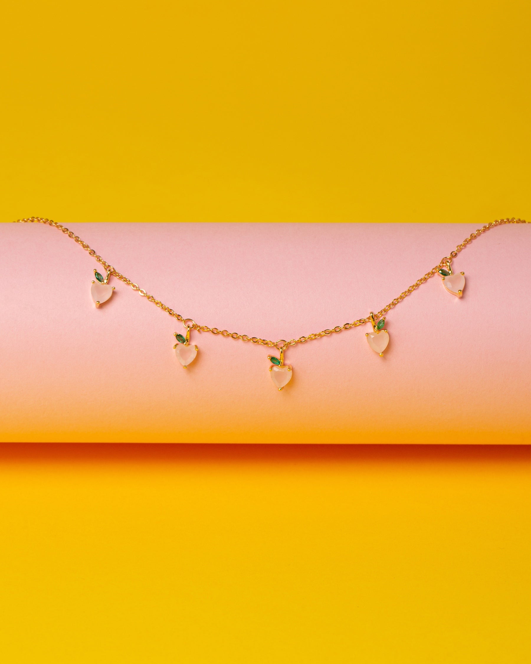 Collana con charms a forma di pesca placcata in oro 18 carati – su sfondo giallo e rosa