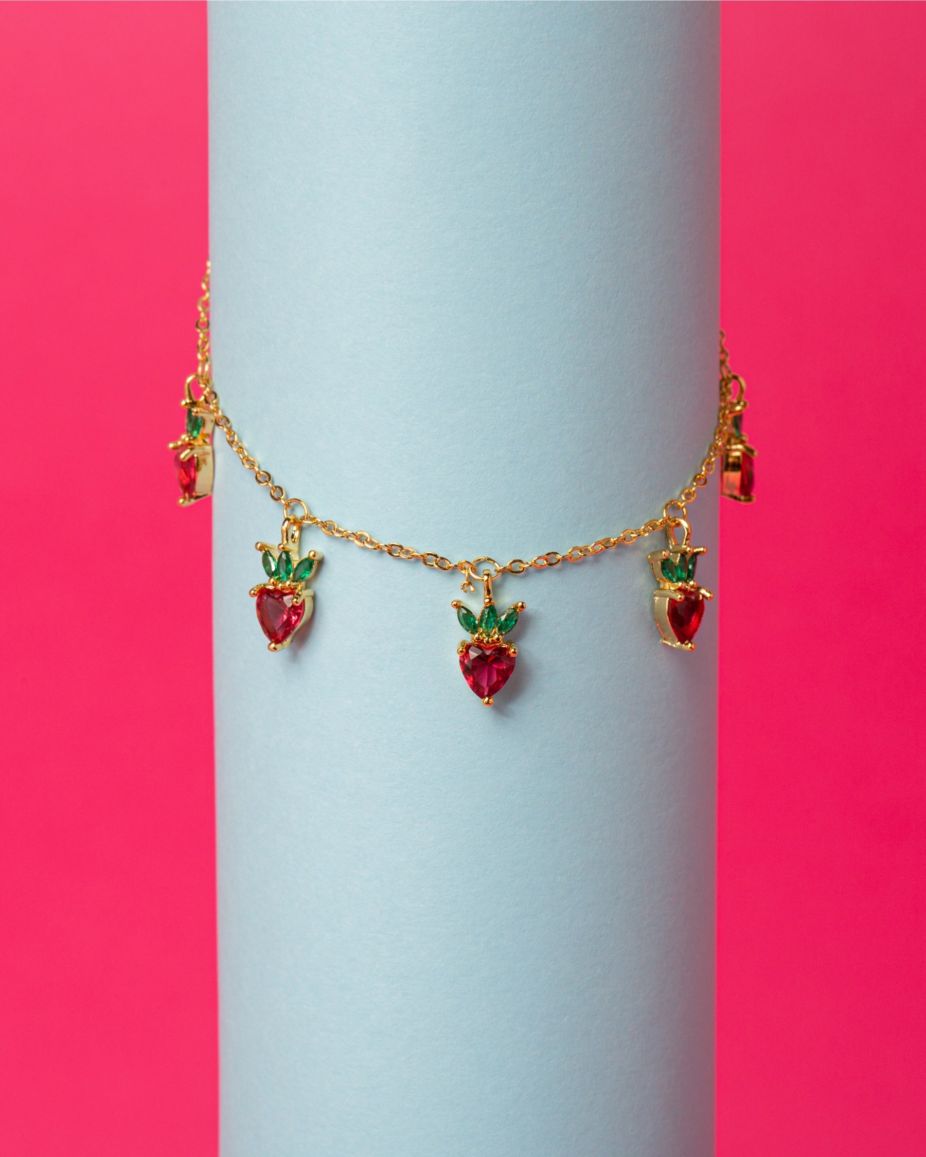 Bracciale charms fragola su sfondo rosa e azzurro – gioiello dorato dal design giocoso di Fruits & Jewels
