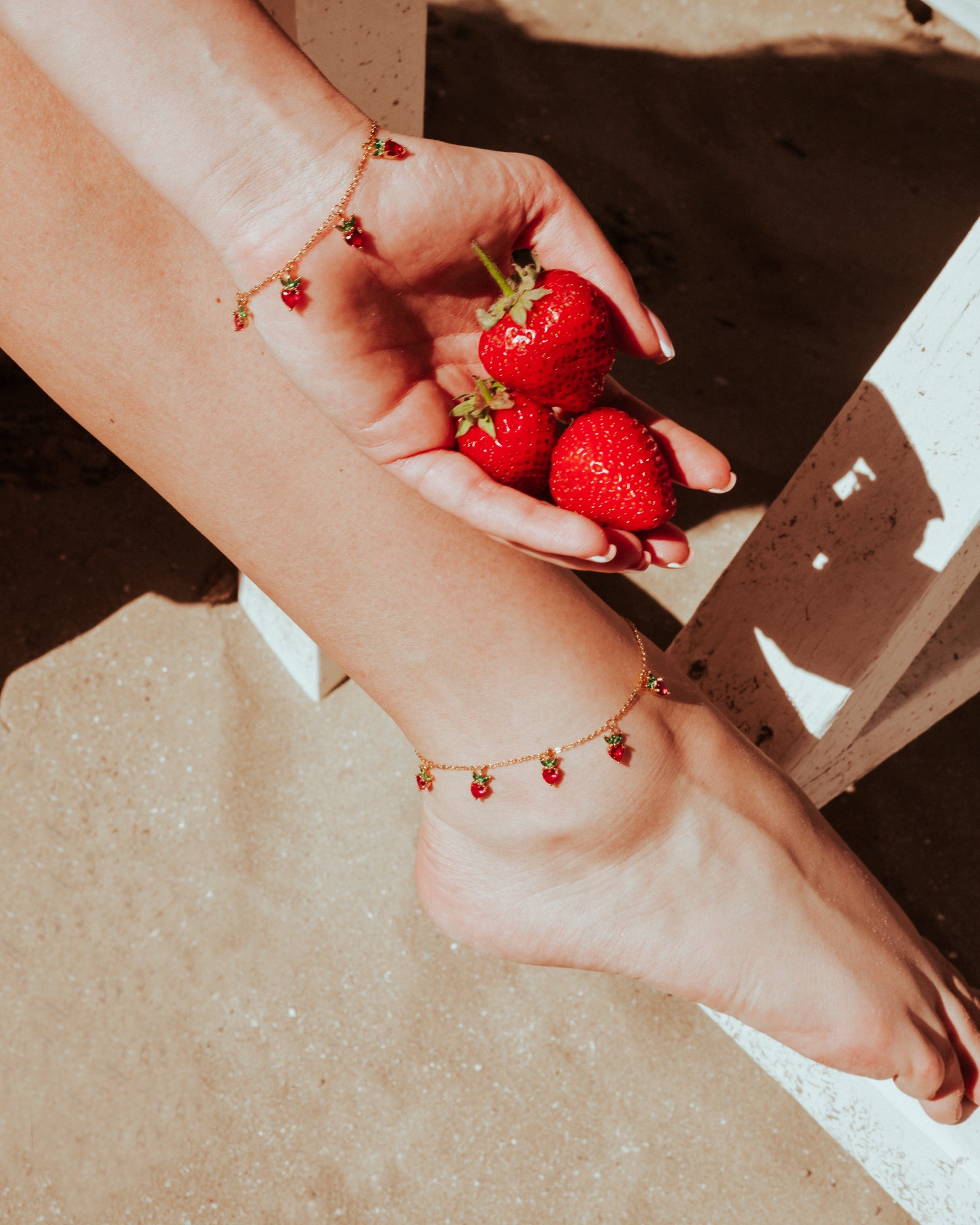 Cavigliera fragola placcata in oro 18k indossata su piede femminile con fragole fresche – gioiello estivo firmato Fruits & Jewels