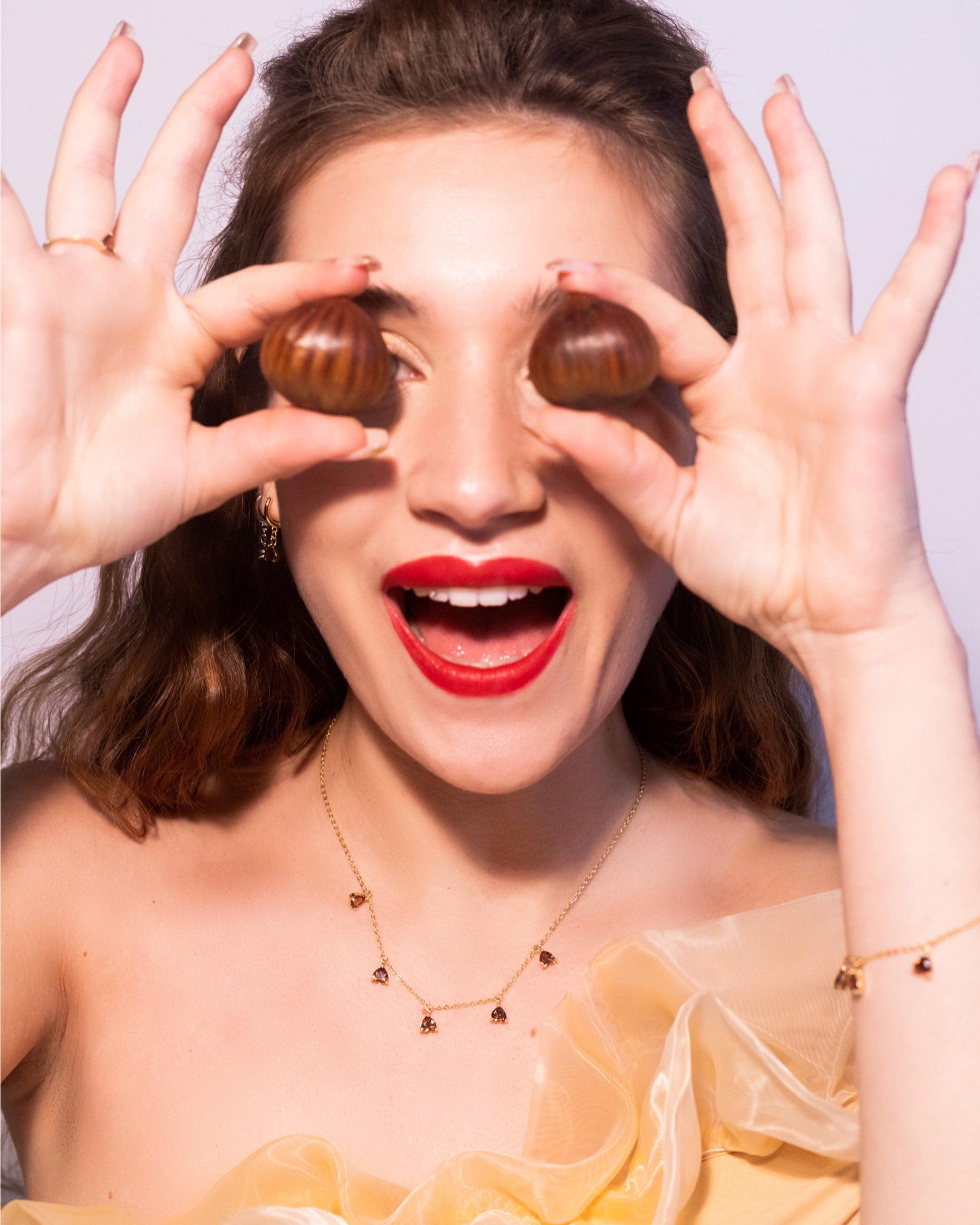 Modella sorridente con collana charms castagna placcata in oro 18 carati Fruits & Jewels, per un look allegro e autunnale dal tocco naturale e luminoso.
