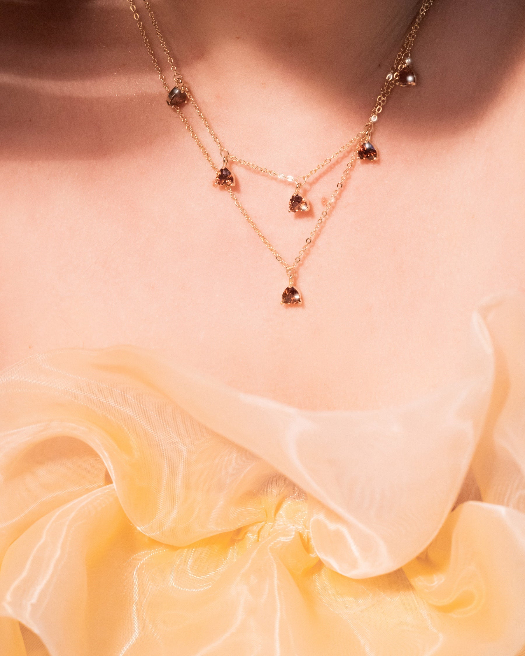 Primo piano della collana pendente castagna Fruits & Jewels in oro 18 carati, indossata sopra un abito color miele. Un tocco raffinato ispirato all’autunno.