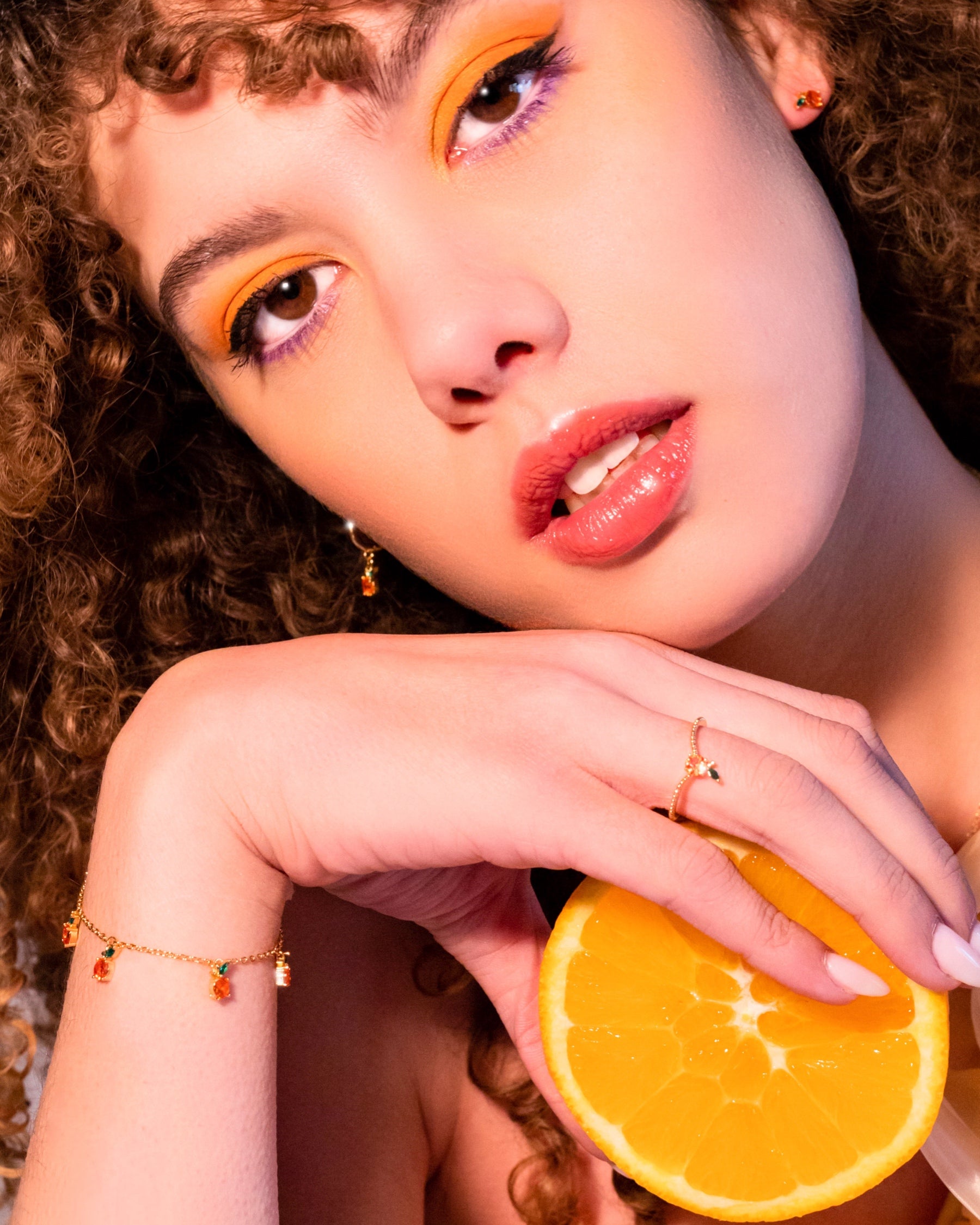 Bracciale arancia placcato oro 18 carati Fruits & Jewels indossato da modella con trucco giallo e fetta d’arancia in primo piano