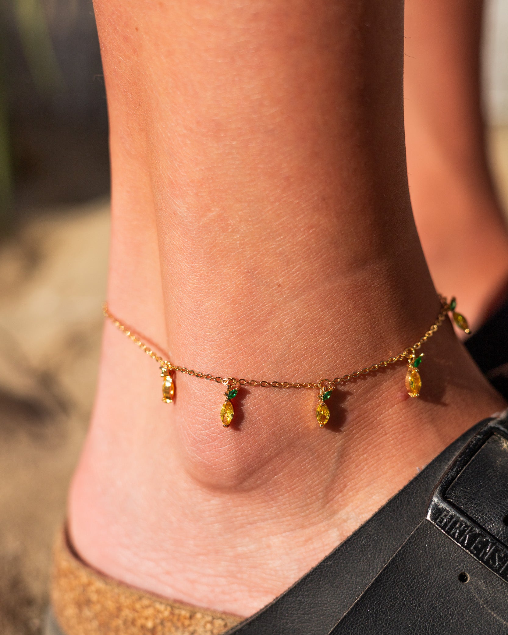 Dettaglio della cavigliera con 5 charms a forma di limone placcati in oro 18k, indossata su piede nudo sulla sabbia – gioiello estivo Fruits & Jewels
