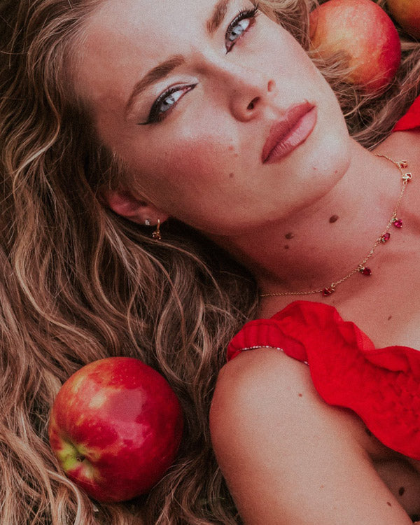Orecchino pendente mela con collana abbinata indossati in posa distesa tra le mele, Fruits & Jewels