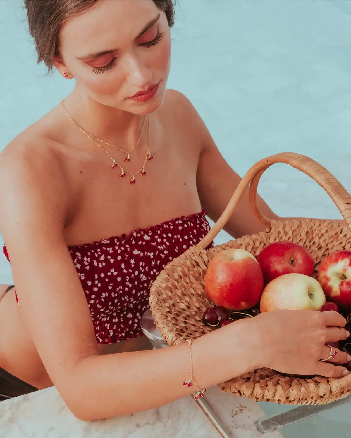 Collana charms ciliegia in oro 18 carati indossata da modella con top a pois e cesta di frutta – stile romantico e retrò by Fruits & Jewels