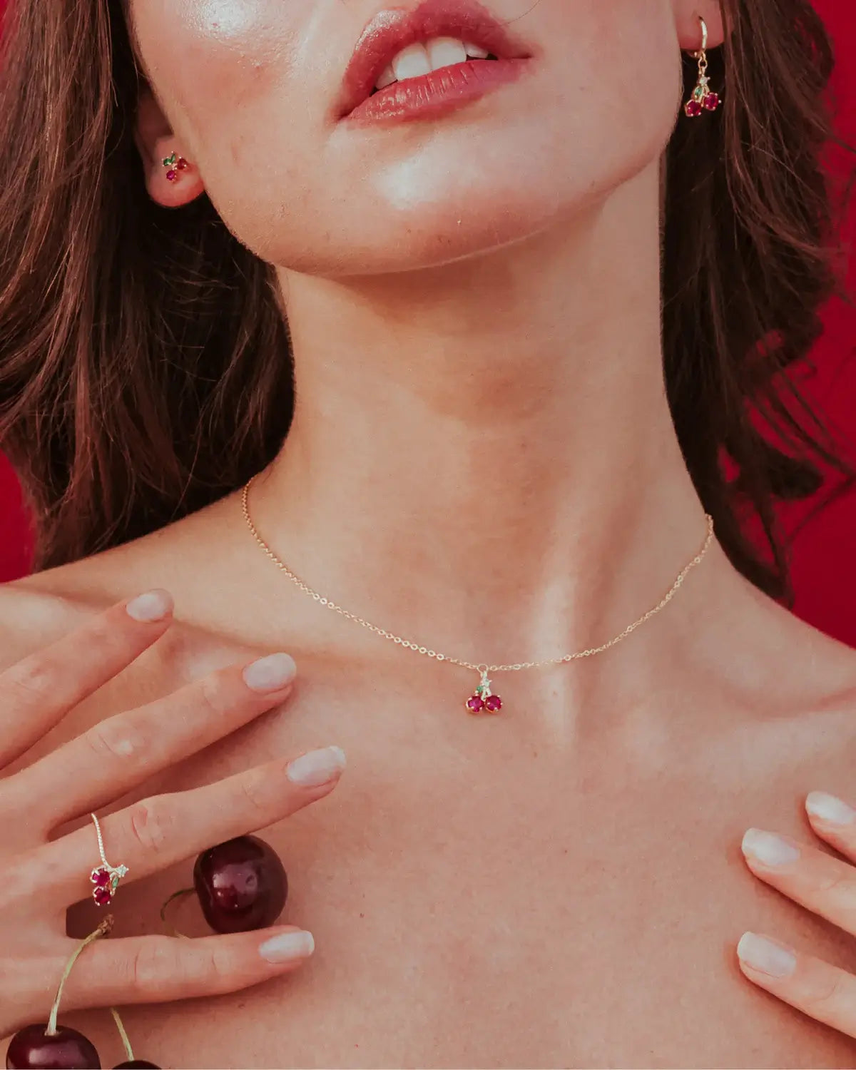 Collana pendente con charm ciliegia in oro 18k indossata da modella – dettaglio fruttato su sfondo rosso Fruits & Jewels