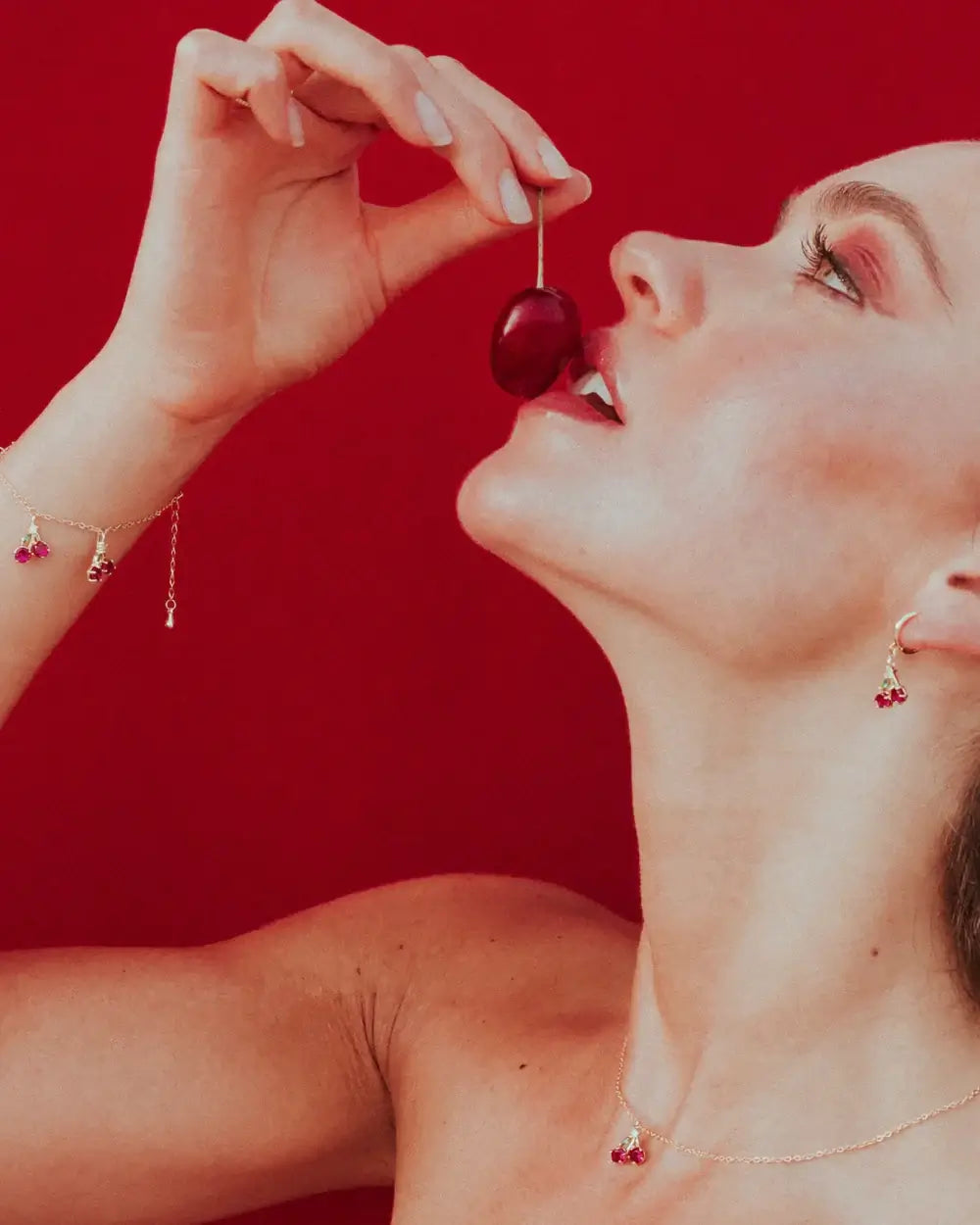 Orecchino ciliegia placcato oro 18 carati visibile mentre la modella porta alla bocca una ciliegia – atmosfera sensuale e fruttata Fruits & Jewels