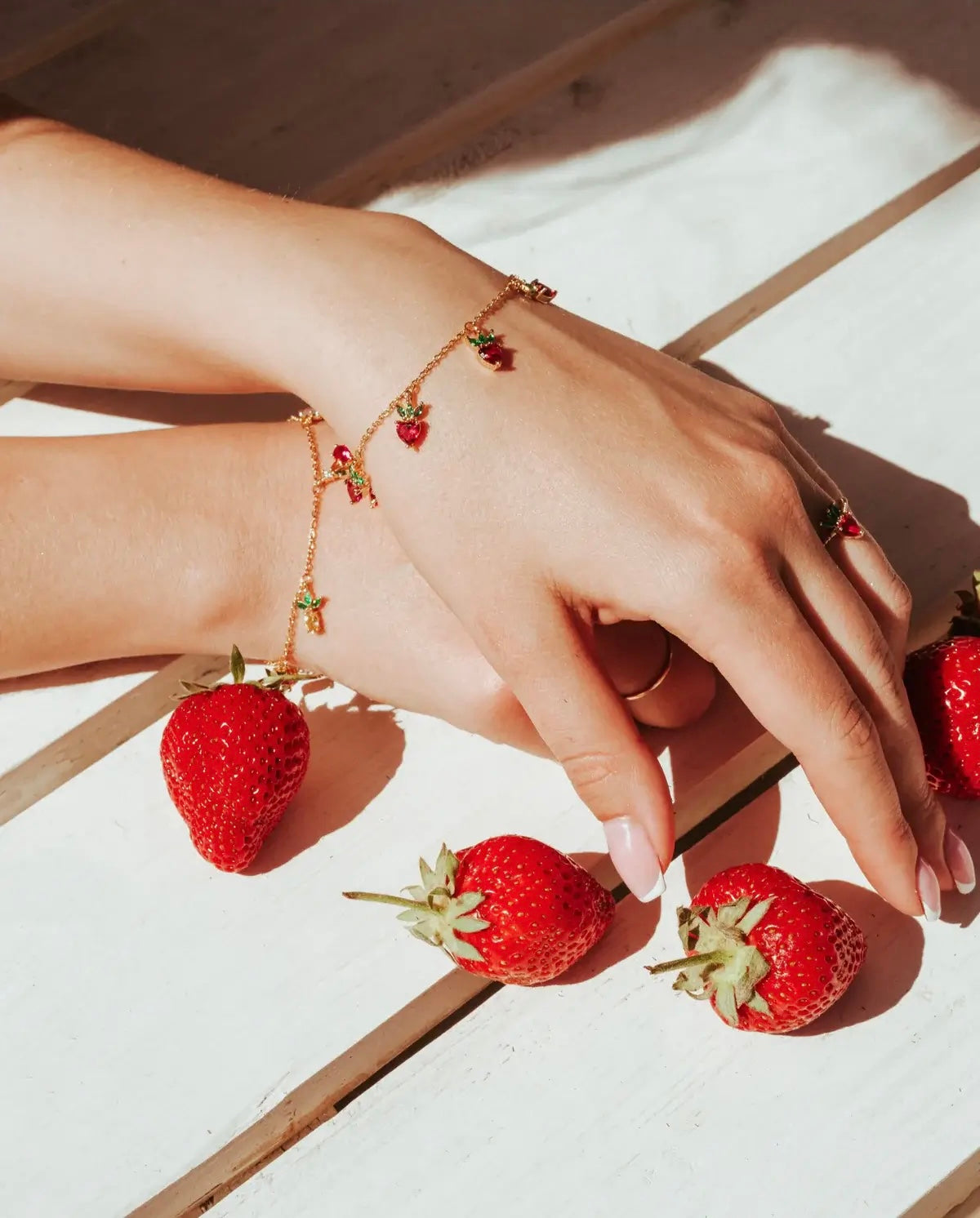 Bracciale charms fragola in oro 18k accanto a fragole fresche – gioiello estivo e fruttato firmato Fruits & Jewels